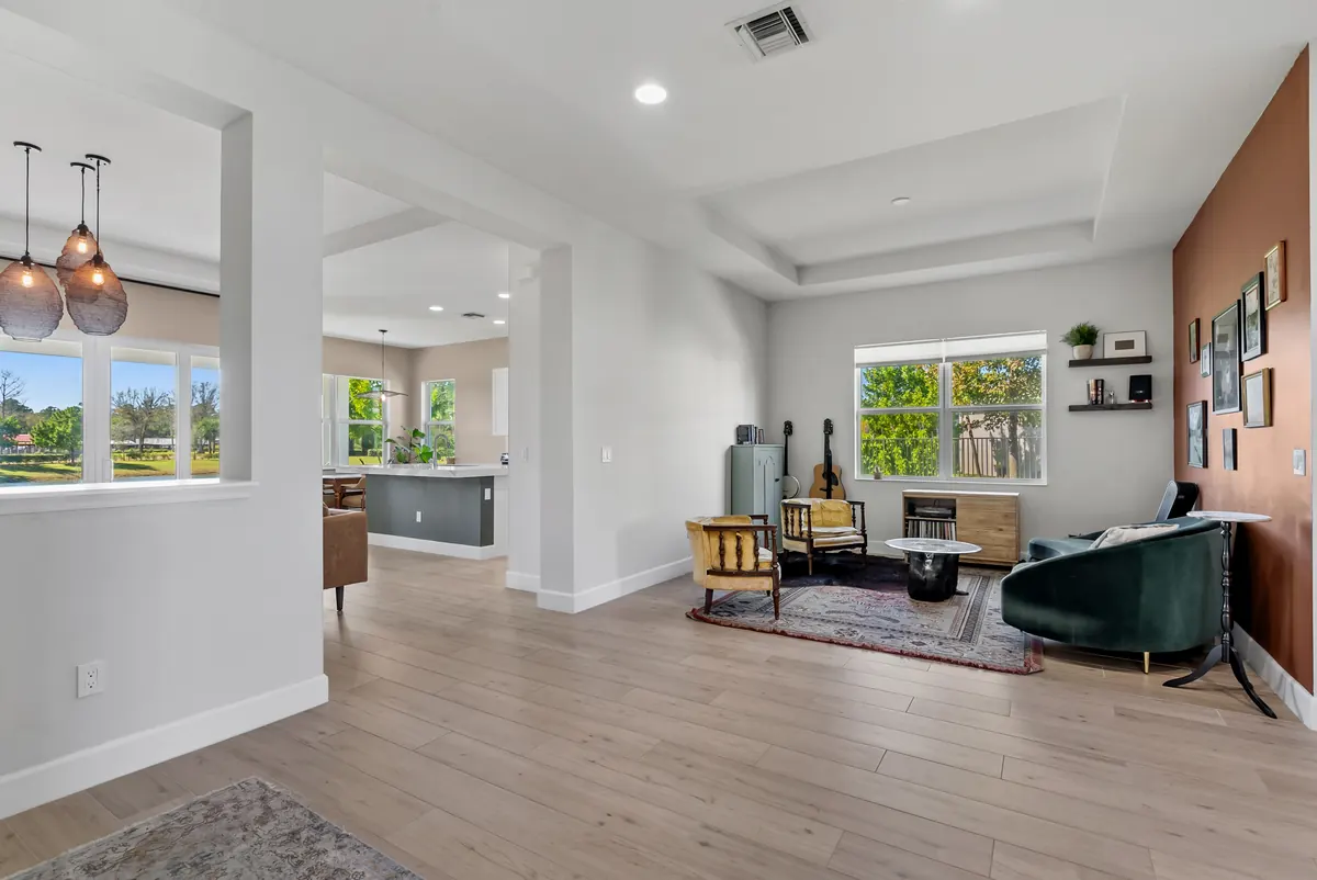 Open living area with green chairs, wood flooring and a view into the kitchen
