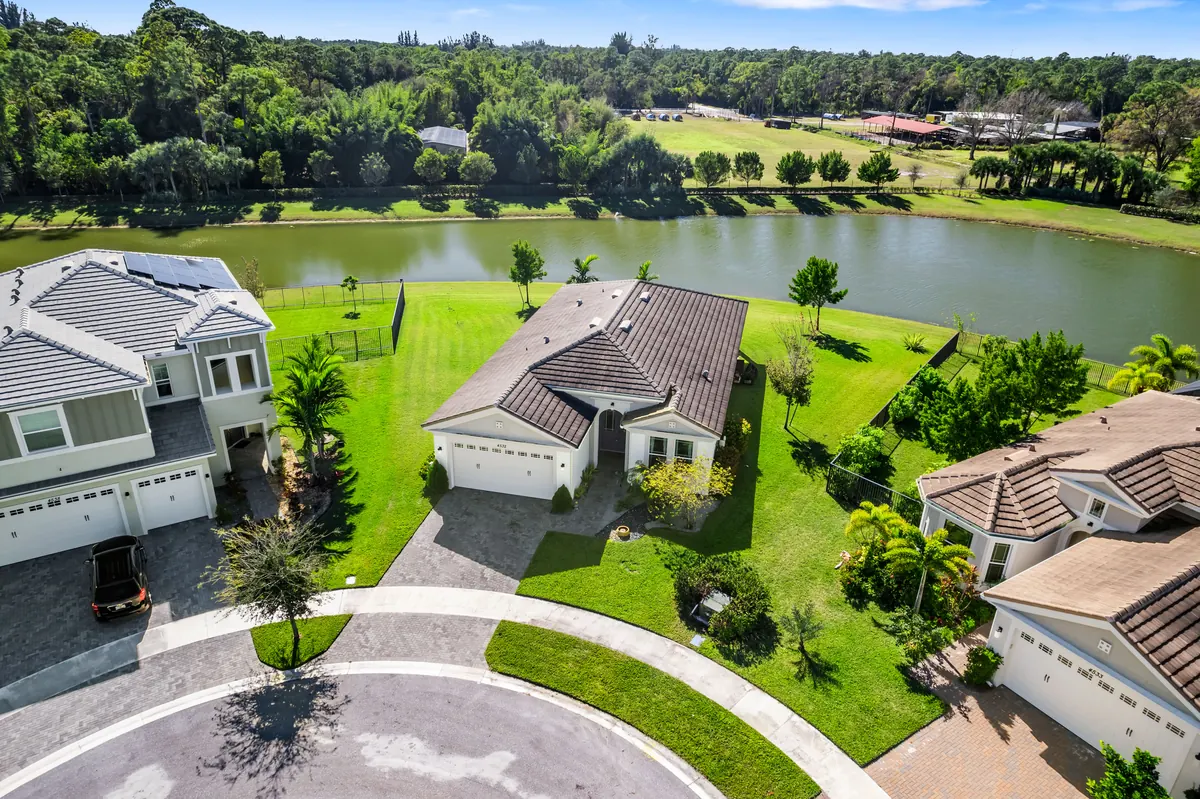 Elevated view of a single-story home on a curved street beside a lake